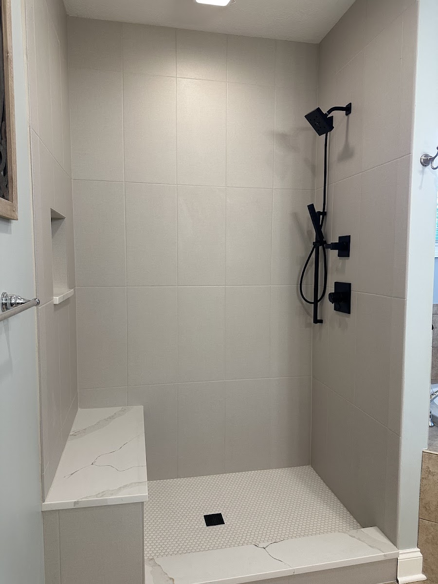 A modern gray-tile shower with matte black fixtures and a marble bench