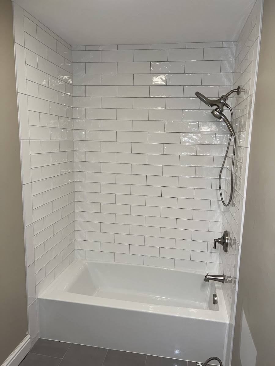 A white subway-tile tub surround with a handheld shower fixture